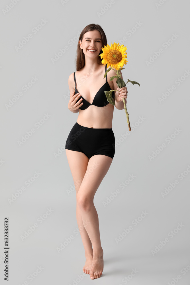 Young happy woman in underwear with beautiful sunflower on grey background