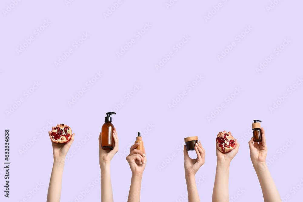 Female hands holding cosmetic products and pomegranate on lilac background