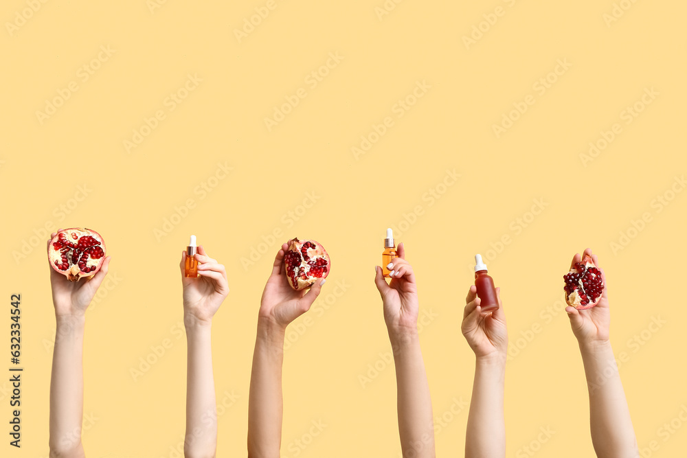 Female hands holding cosmetic products and pomegranate on yellow background