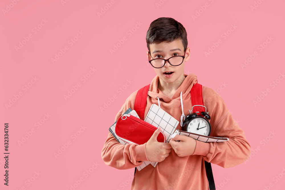 Portrait of shocked schoolboy with school supplies and alarm clock on pink background