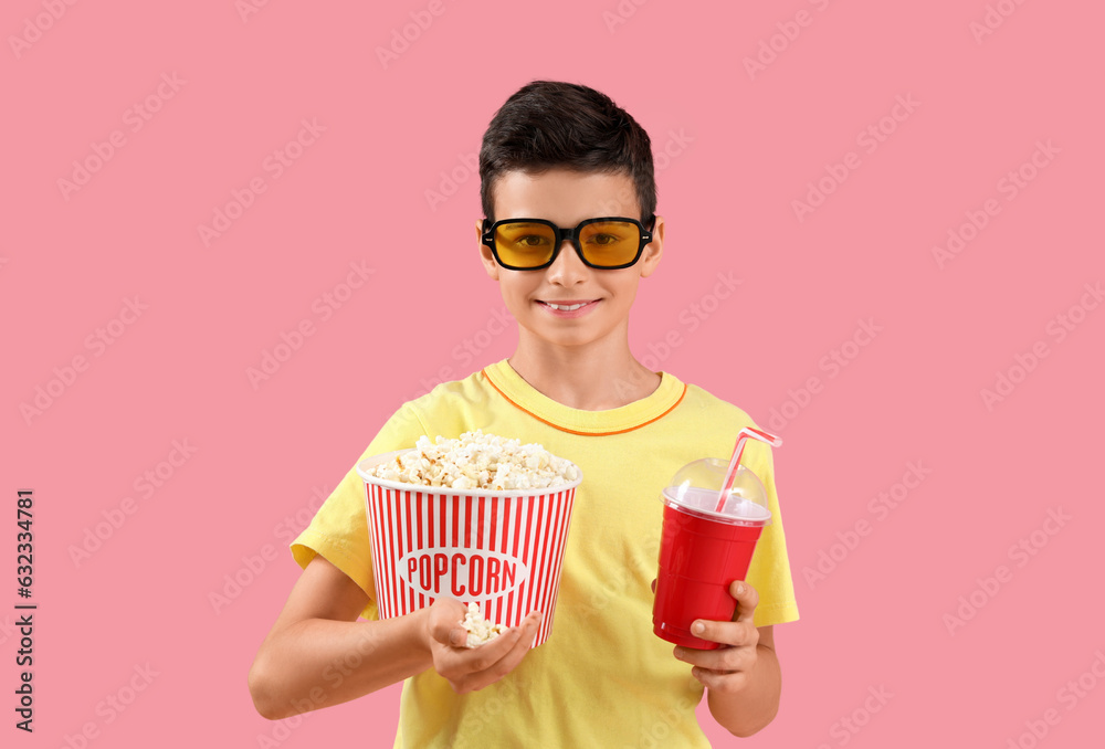 Cute little boy in 3D glasses with popcorn and drink on pink background