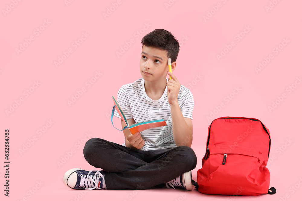 Portrait of thoughtful schoolboy with backpack sitting on pink background