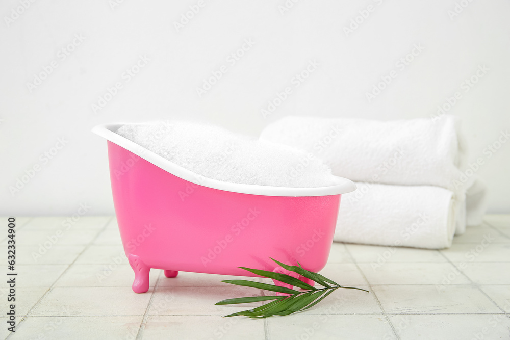 Small bathtub with foam, clean towels and palm leaf on light tile table