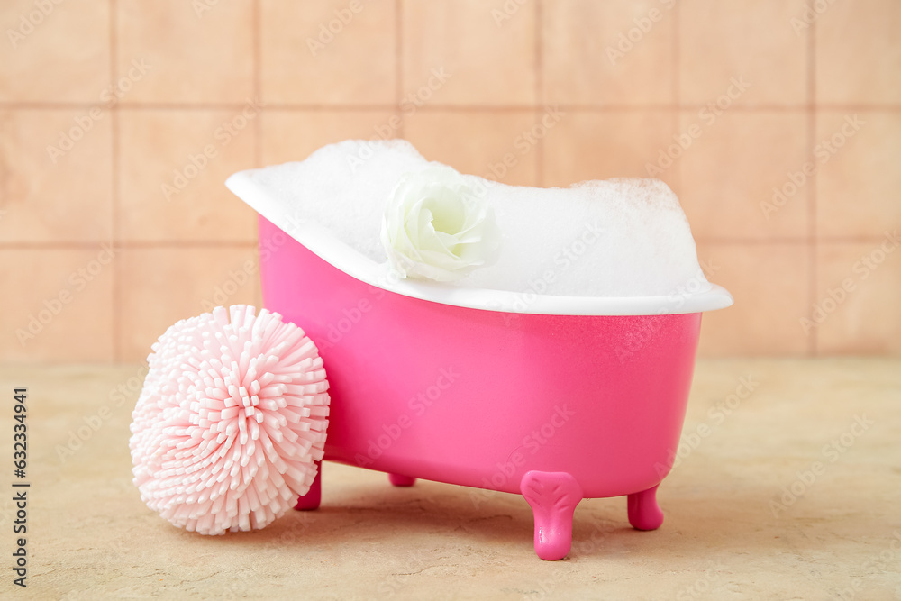 Small bathtub with soap foam and sponge on color background