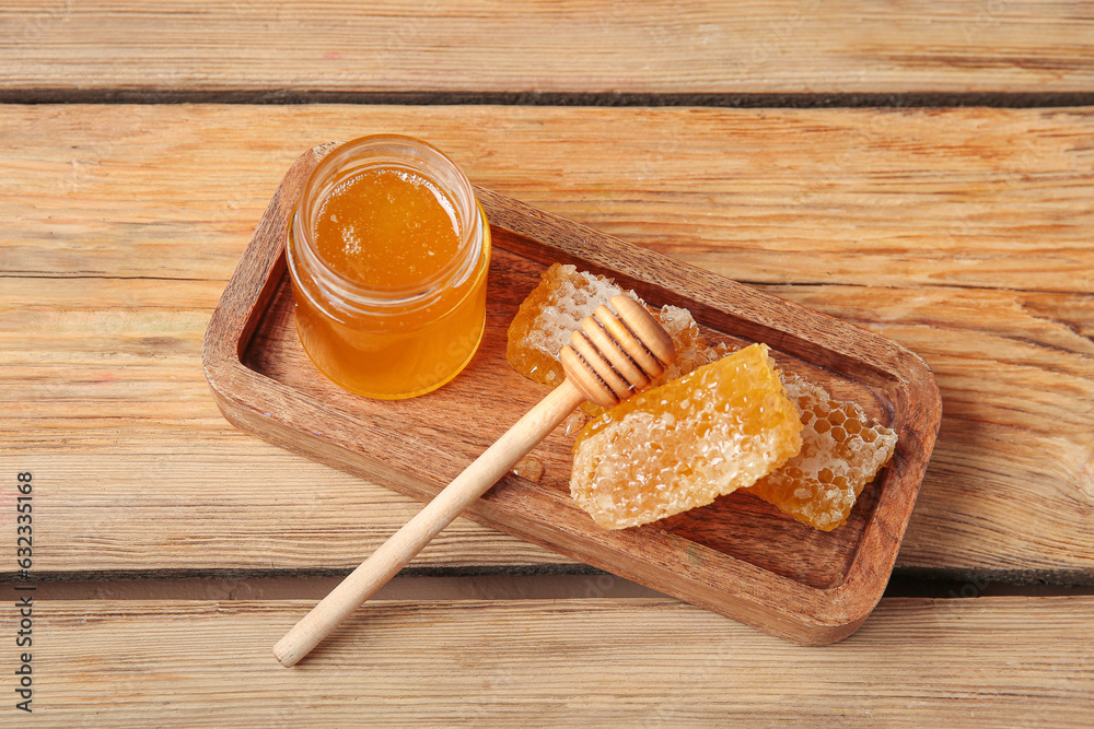 Board with jar of tasty honey and combs on wooden background