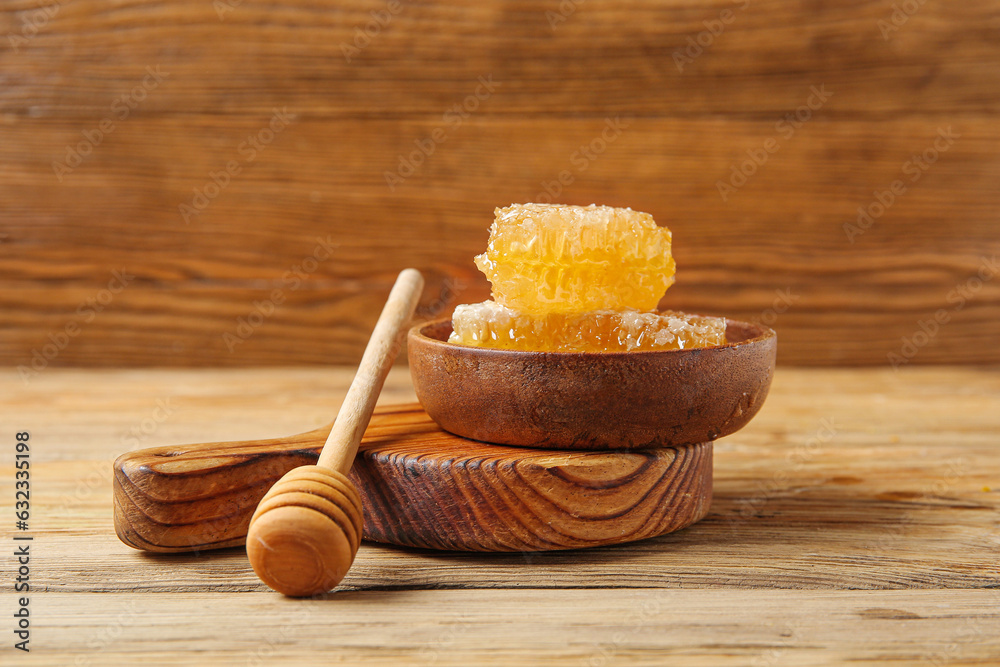 Bowl with sweet honeycombs and dipper on wooden background