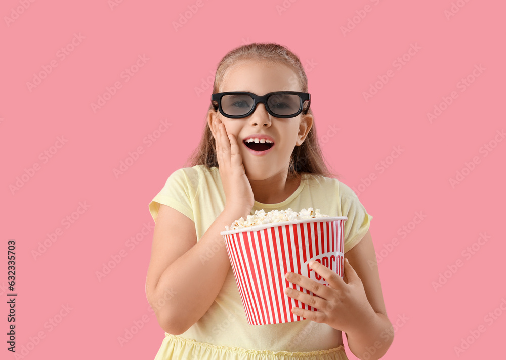 Surprised little girl in 3D cinema glasses with popcorn bucket on pink background