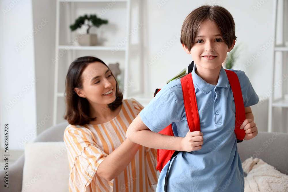 Mother putting notebooks in backpack of her little boy at home