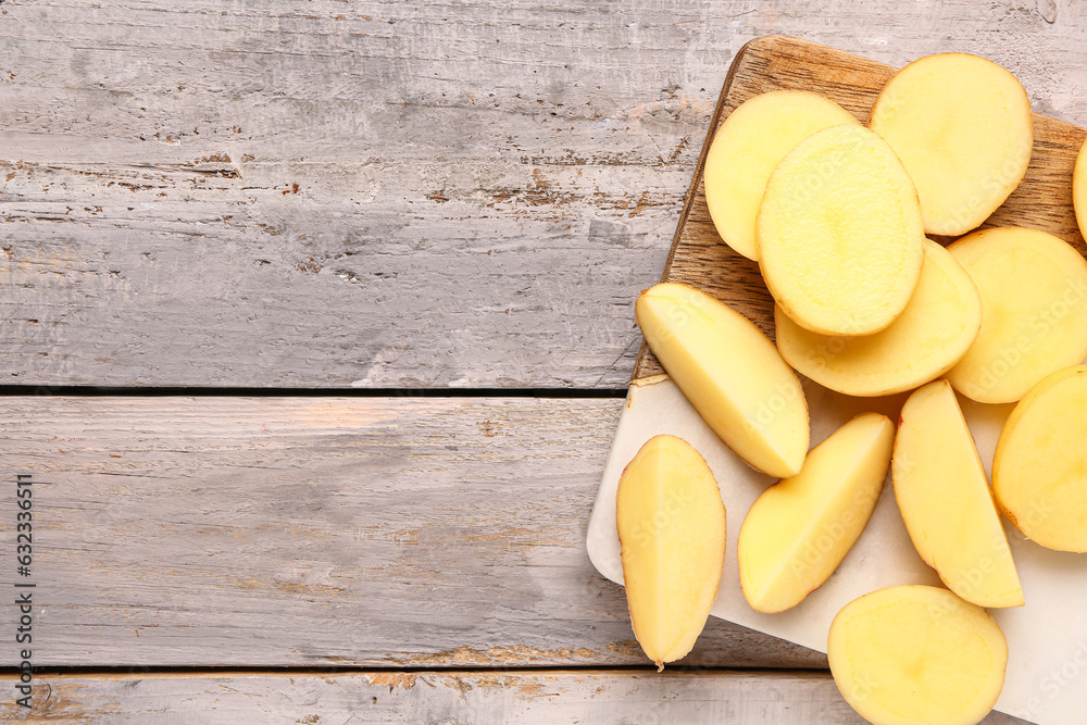 Board with slices of fresh raw potatoes on grey wooden background