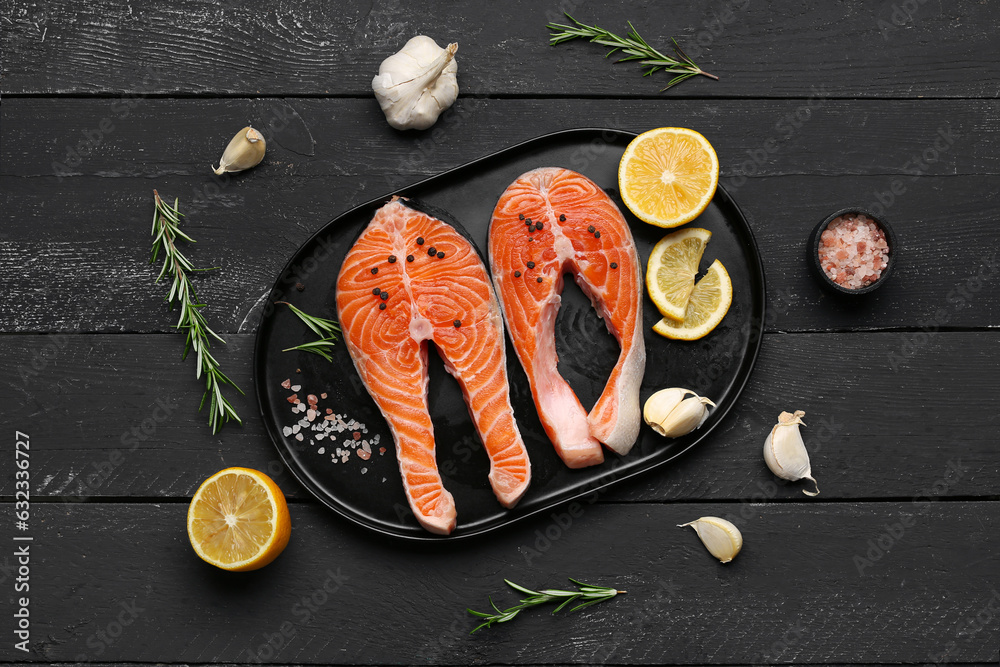 Plate with raw salmon steaks and different spices on black wooden background