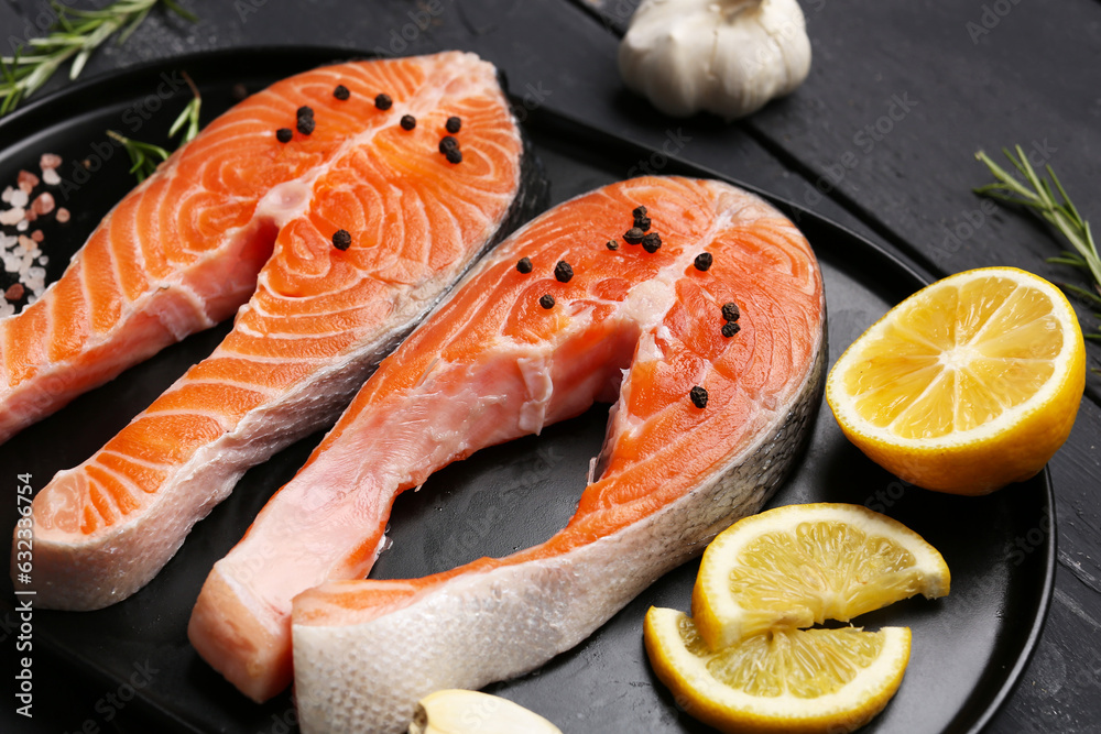 Plate with raw salmon steaks and different spices on black wooden background