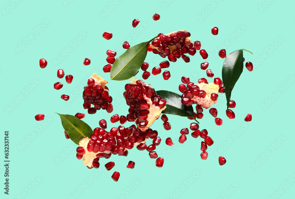 Flying fresh pomegranates with seeds and leaves on turquoise background