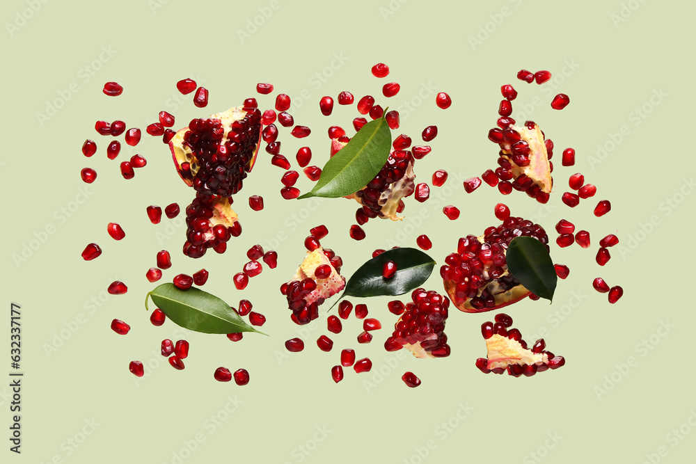 Flying fresh pomegranates with seeds and leaves on green background