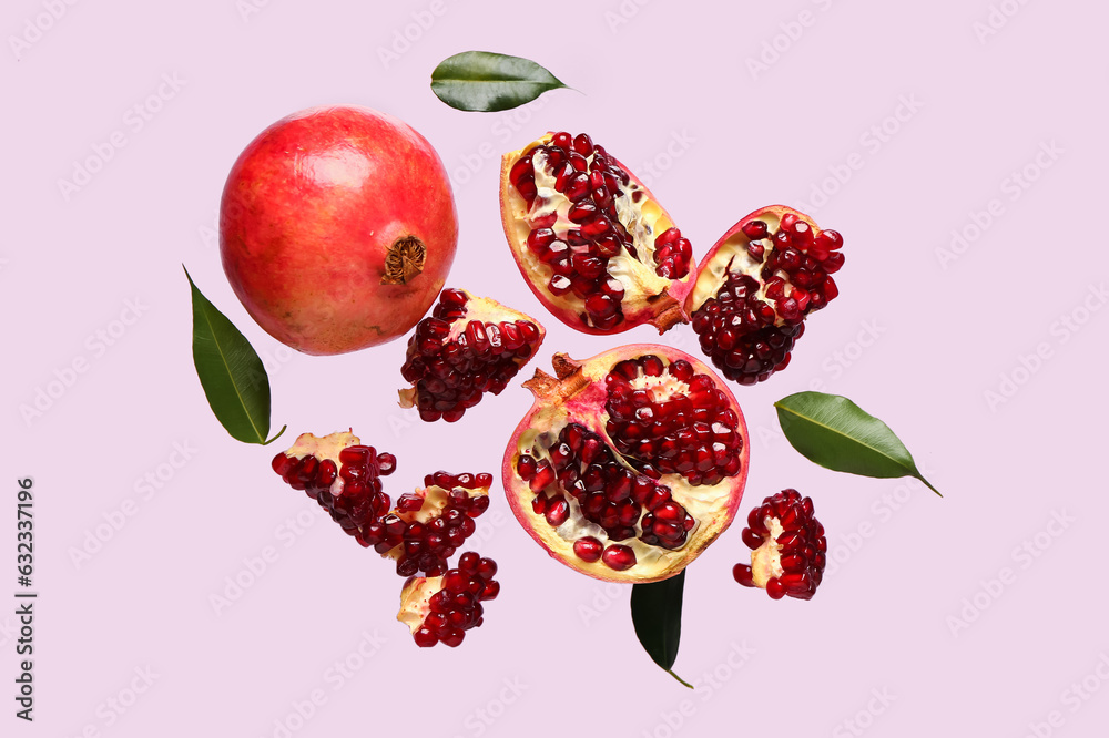 Flying fresh pomegranates and leaves on lilac background