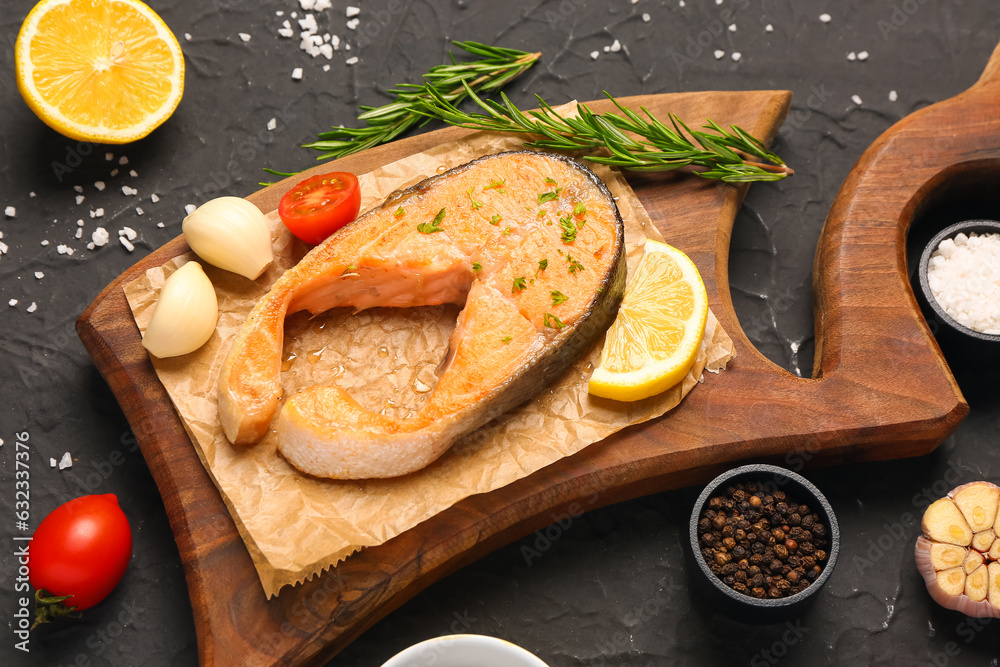 Wooden board of tasty salmon steak with tomatoes, garlic and lemon on black background