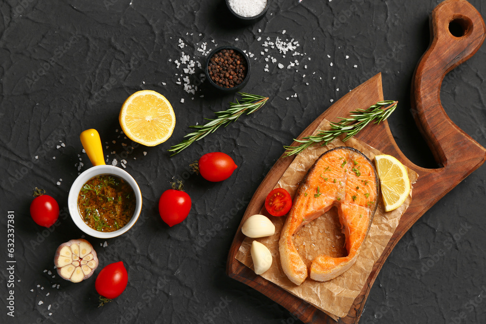 Wooden board of tasty salmon steak with tomatoes and lemon on black background