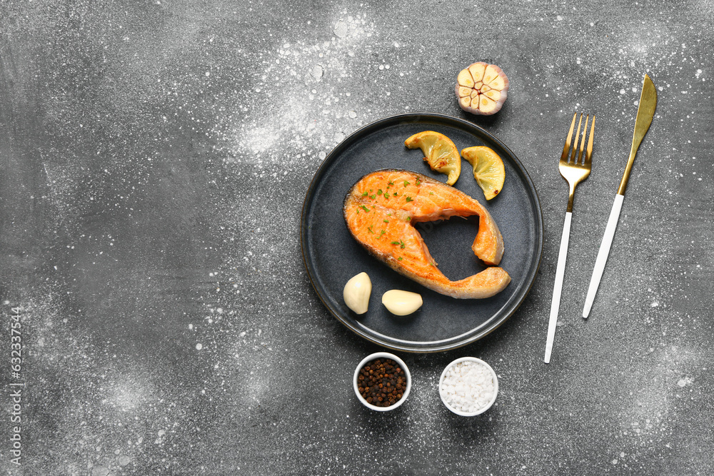 Plate of tasty salmon steak with lemon and garlic on grey background