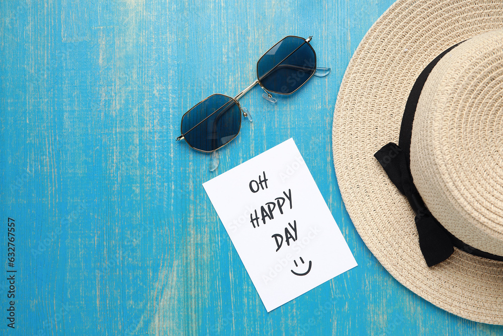 Stylish sunglasses with hat and paper sheet with text OH HAPPY DAY on blue wooden background