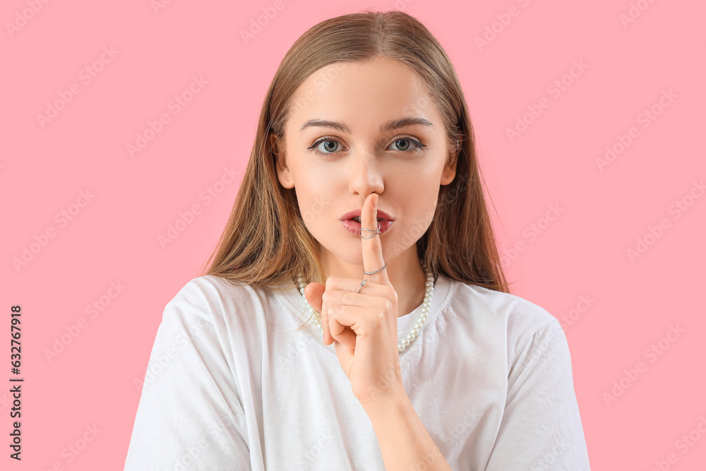 Young woman showing silence gesture on pink background, closeup