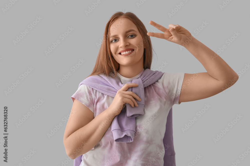 Beautiful redhead woman showing two fingers on grey background