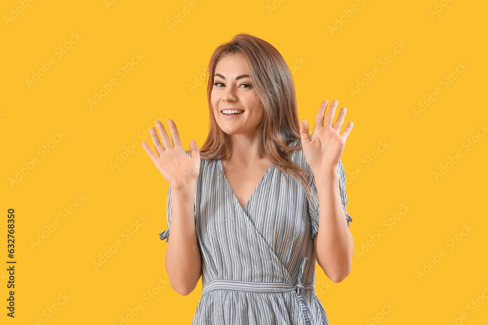 Beautiful woman in striped dress showing hands on yellow background