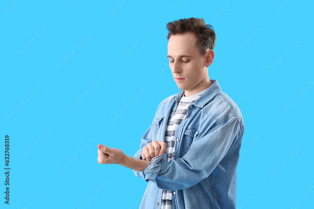 Young man rolling up his sleeve on light blue background