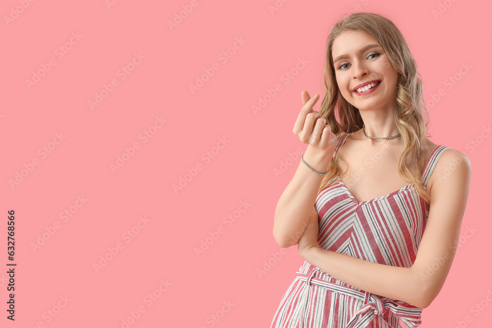 Young woman making heart with her fingers on pink background