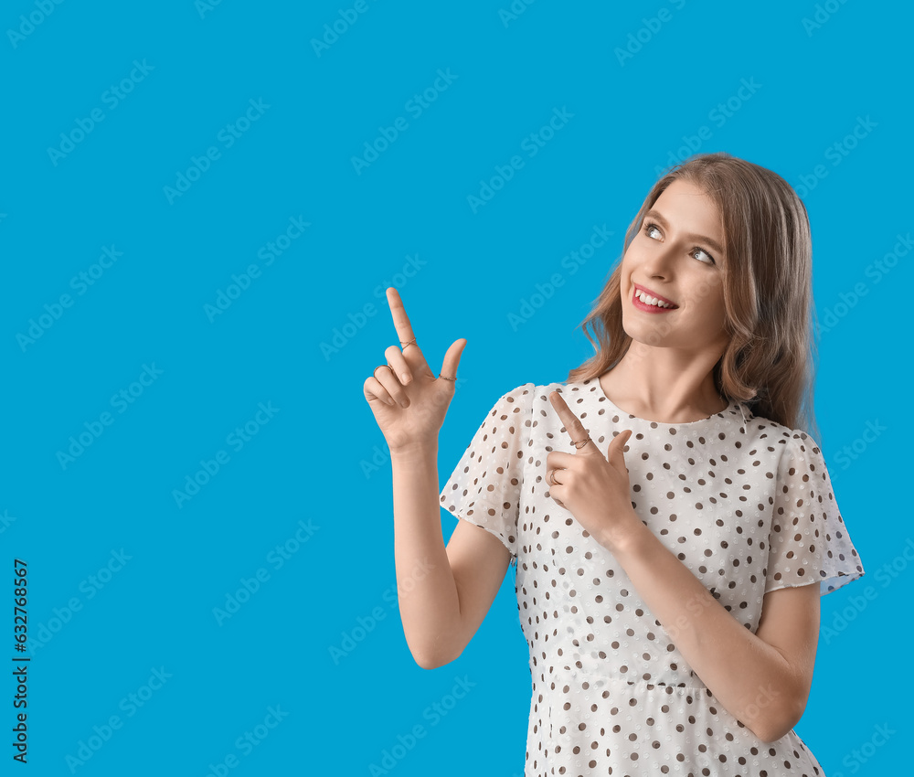 Young woman pointing at something on blue background