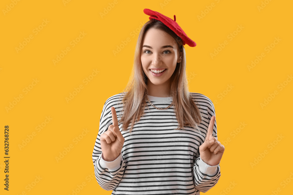 Young woman pointing at something on yellow background