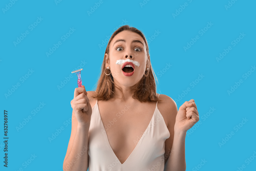 Shocked young woman with shaving foam and razor on blue background, closeup