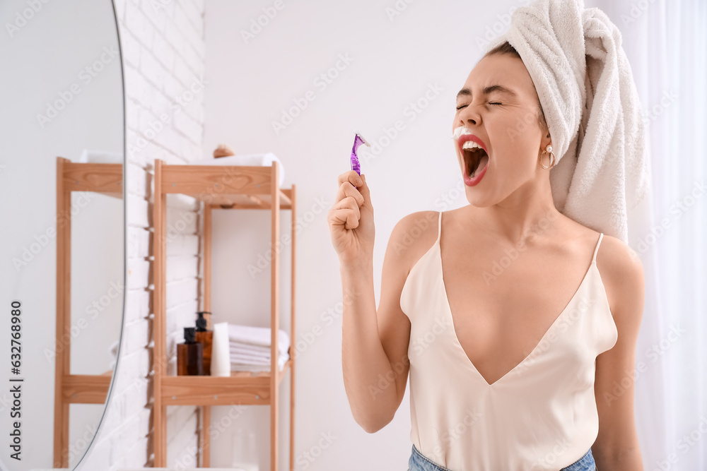 Angry young woman shaving face with razor in bathroom