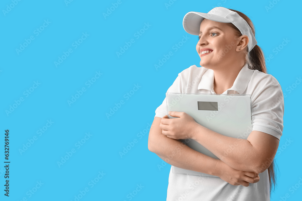 Happy young overweight woman with scales on blue background