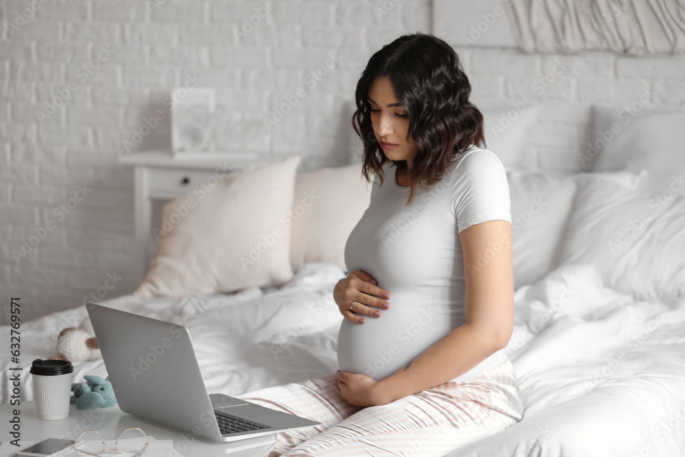 Young pregnant woman working with laptop in bedroom