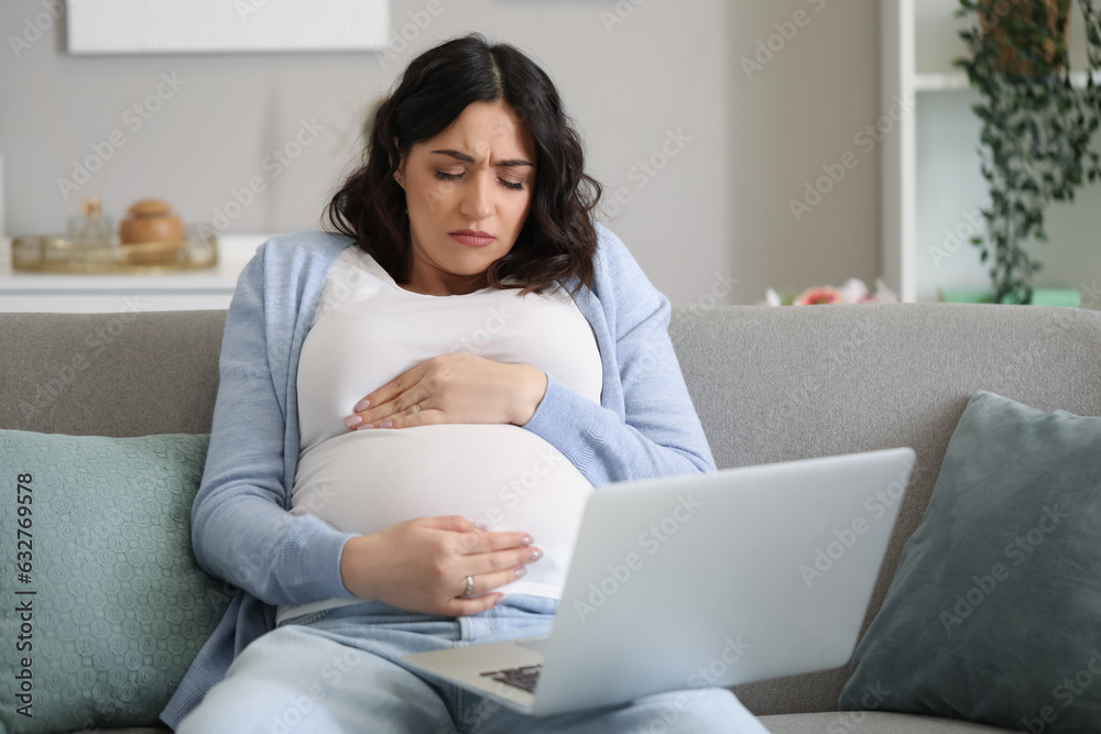 Tired young pregnant woman working with laptop at home