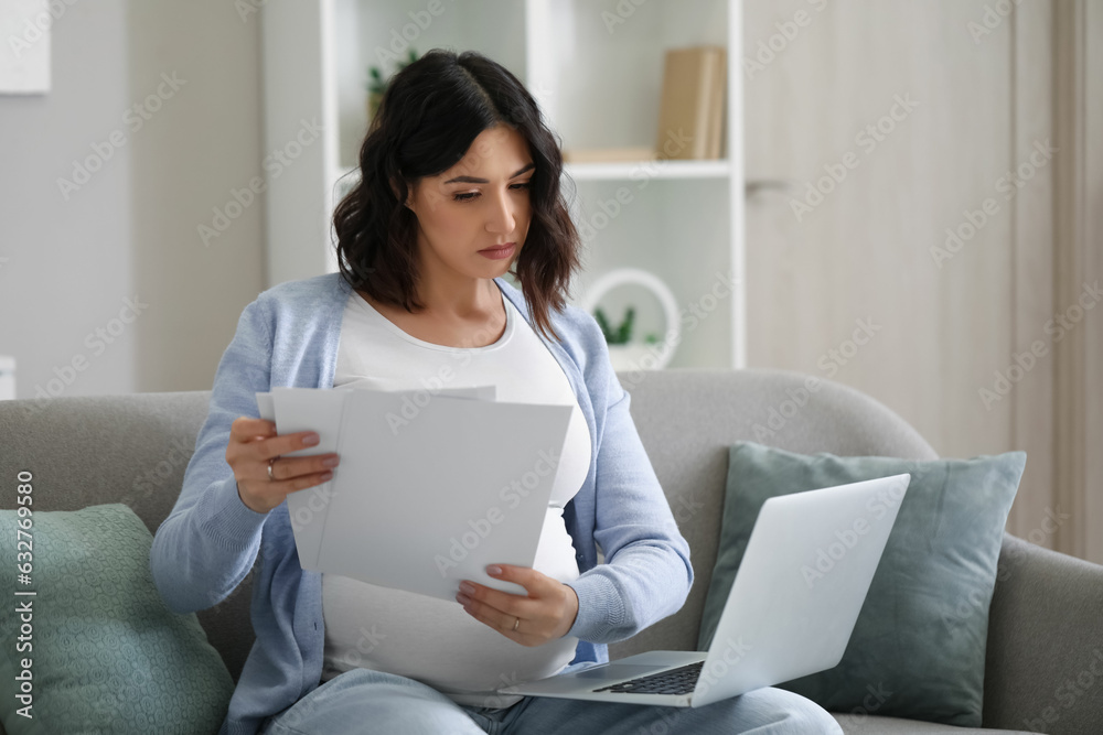 Young pregnant woman working with documents and laptop at home