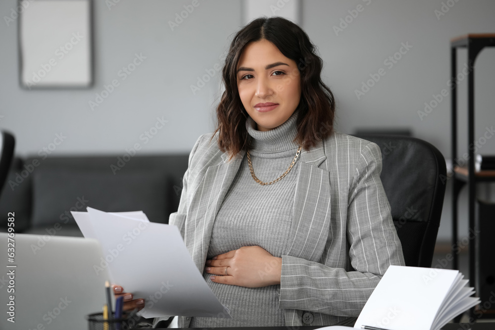 Young pregnant woman working with documents at table in office