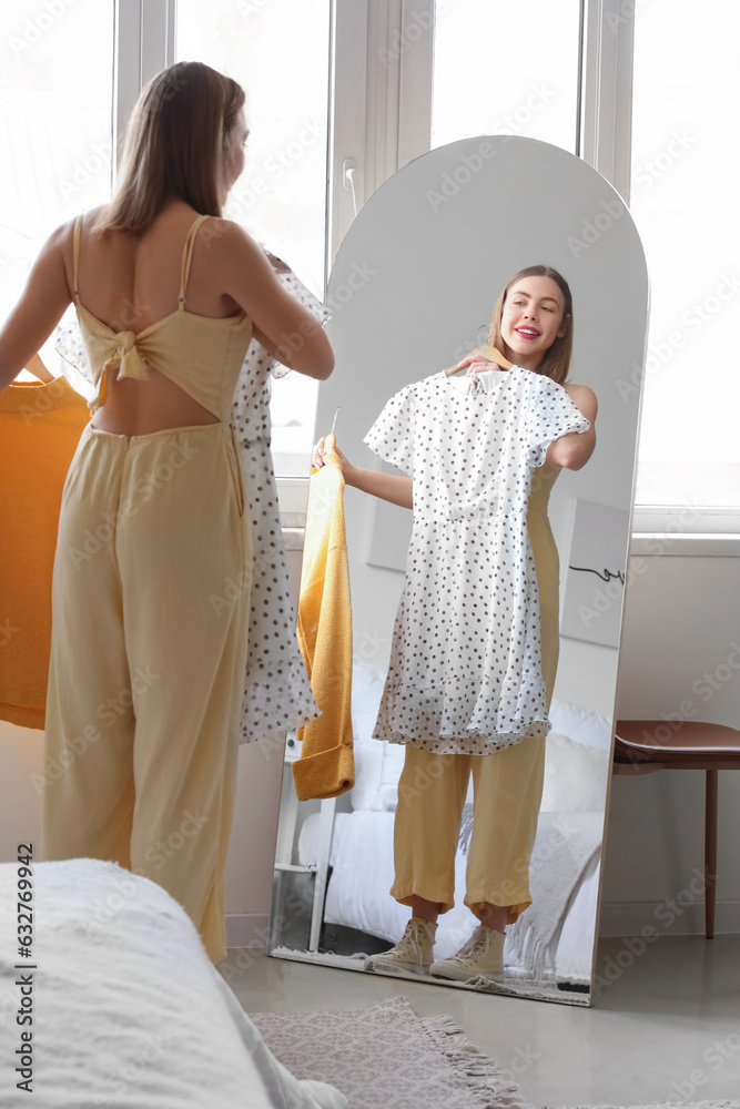 Young woman choosing clothes in front of mirror at home