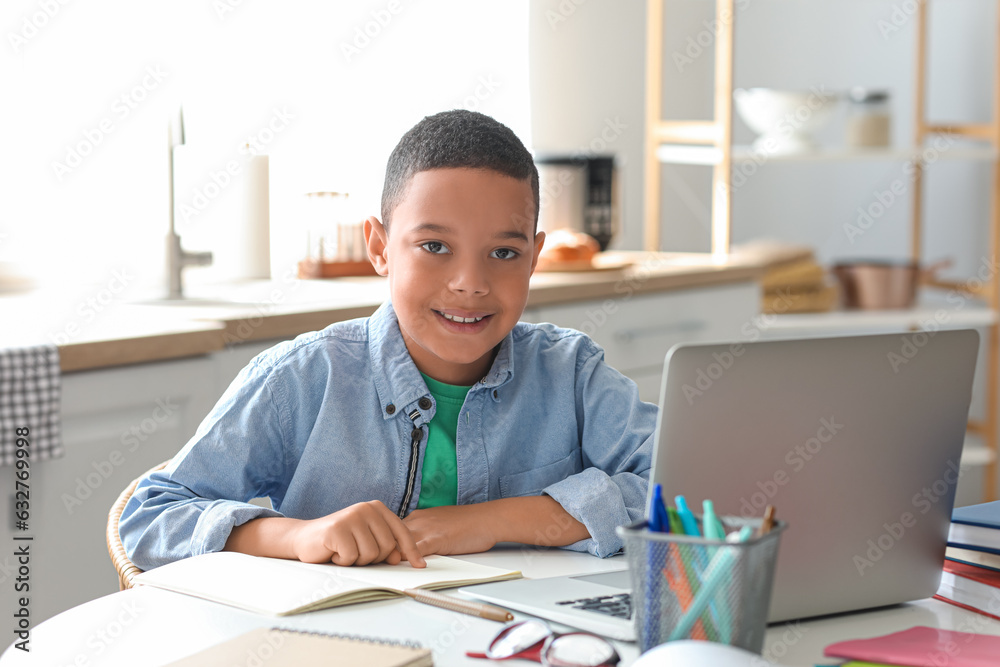 Little African-American boy studying computer sciences online in kitchen