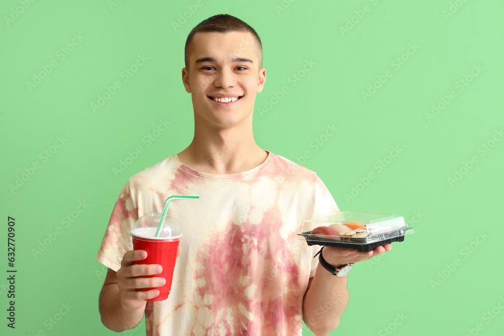 Young man with tasty sushi and drink on green background