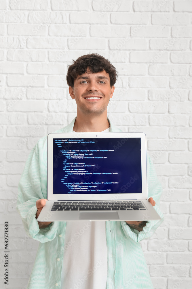 Male programmer working with laptop on white brick background