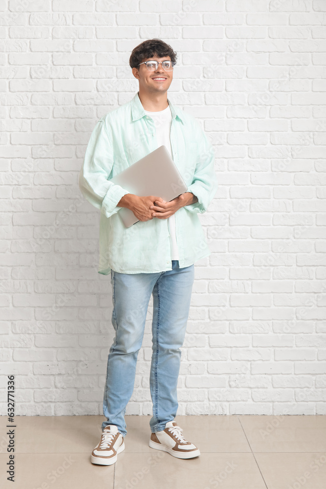 Male programmer with laptop near white brick wall