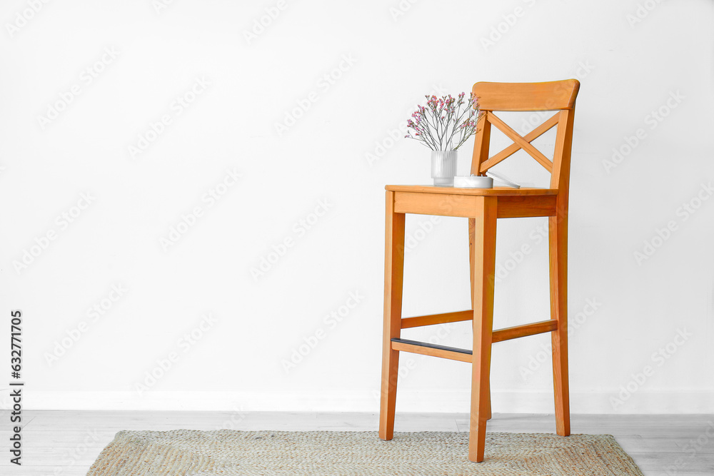 Beautiful flowers and candle on chair near light wall in room