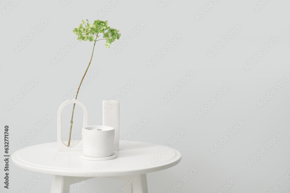 Hydrangea flowers and candle on table near light wall in room