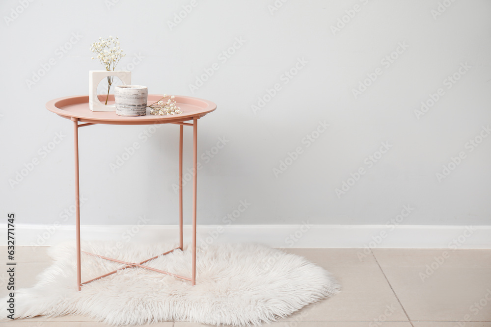 Gypsophila flowers and candle on table near light wall in room