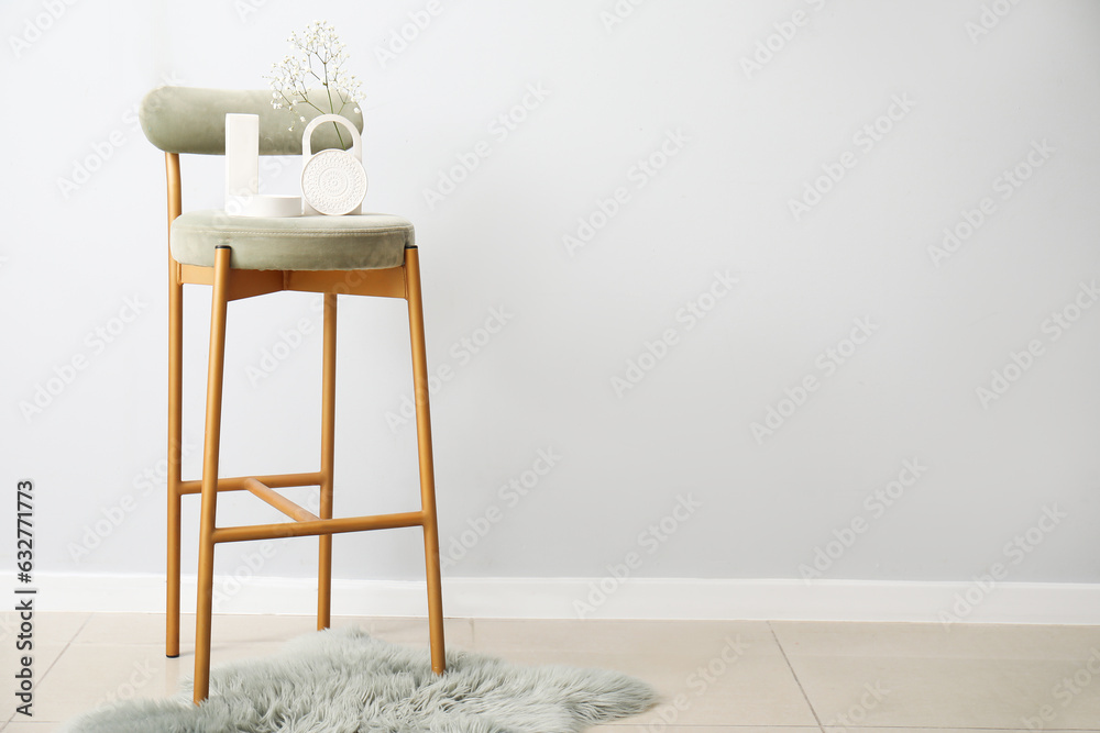 Gypsophila flowers and candle on chair near light wall in room