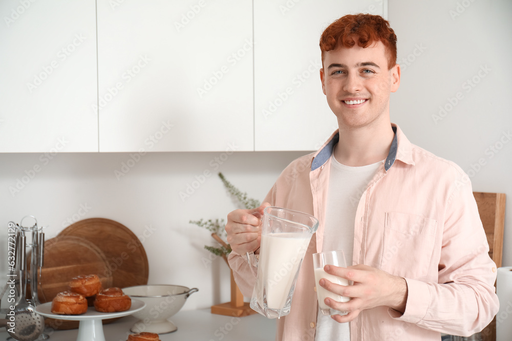 Young redhead man pouring milk into glass in kitchen