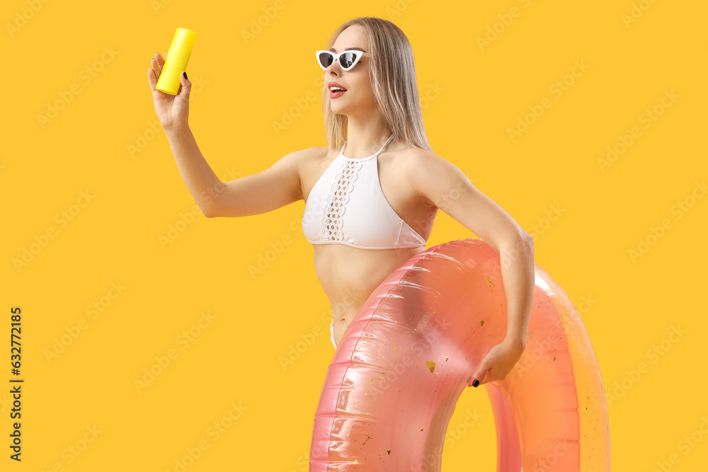 Young woman with sunscreen cream and inflatable ring on yellow background