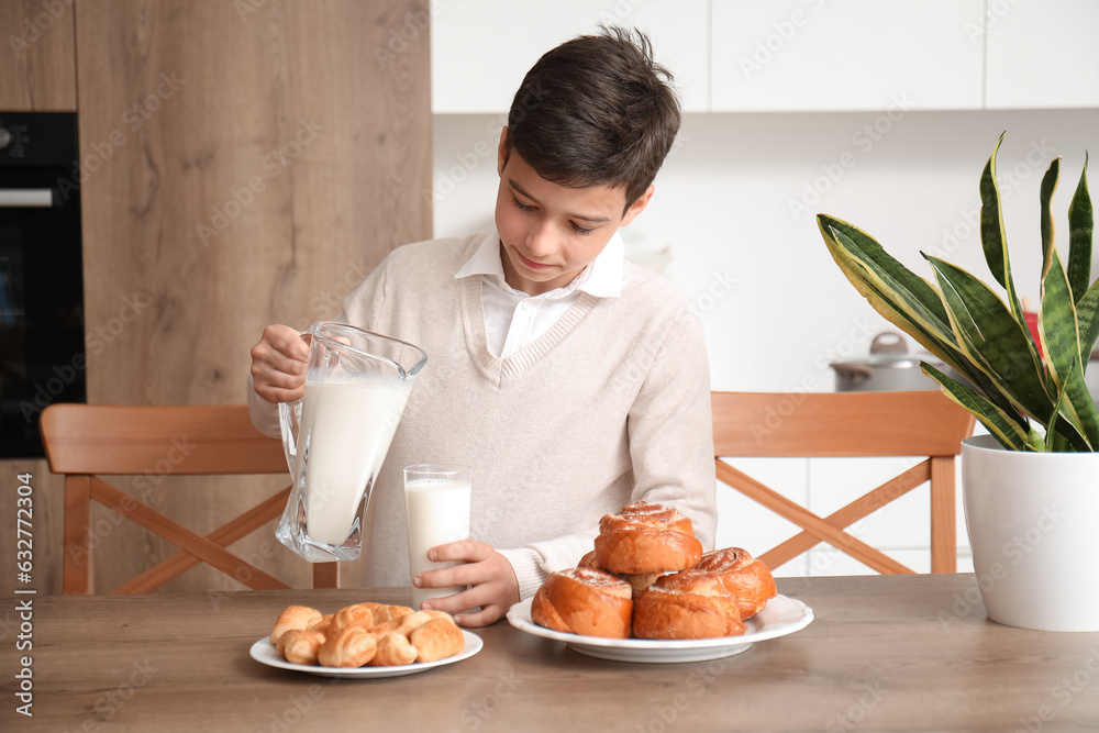 Little boy pouring milk into glass in kitchen