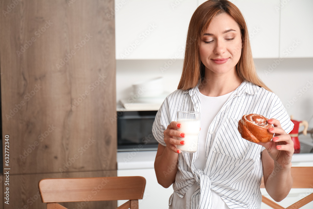 Young woman with glass of milk and tasty bun in kitchen