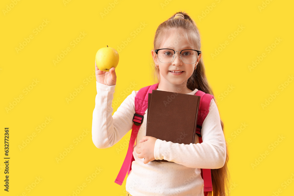 Little schoolgirl with books and apple on yellow background